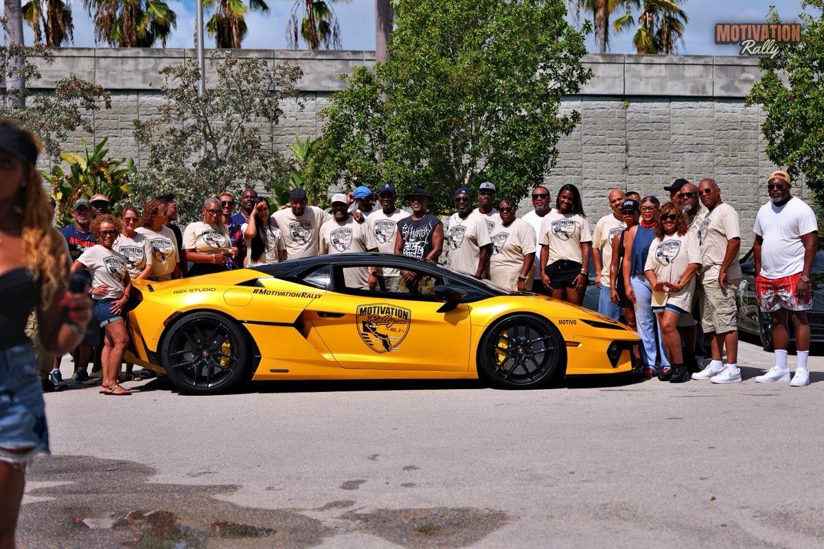 The rally group in Motivation Rally shirts standing behind a yellow Lamborghini in the sun.