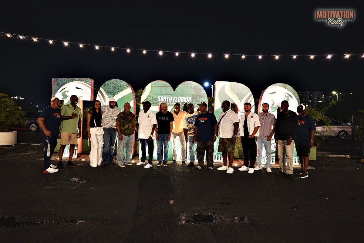 The rally group at night in front of a lit South Florida sign, under a string of lights.