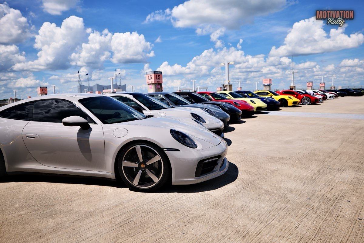 A long row of Porsches on a rooftop parking deck, a silver 911 nearest the camera.