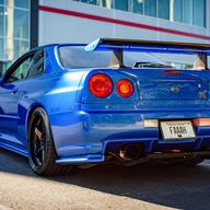 A Bayside Blue Nissan Skyline R34 GT-R from behind, its Montana plate marked PERM for permanent registration.